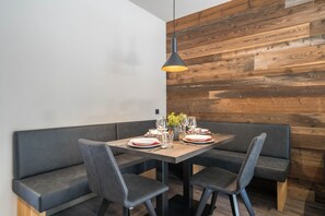 A dining area with a wooden wall, dark seating, and a table set with plates, glasses, and a small plant. - Apartment “Seebrunn - Kaserfeld Alm” with Mountain View, Terrace & Garden (Ulten)