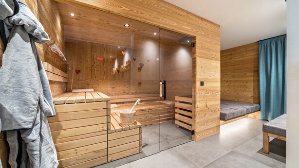 A sauna room with wooden benches, a glass door, and a towel rack. - Apartment “Seebrunn - "Äußere Schwemmalm” with Mountain View, Wi-Fi and Sauna (Ulten)