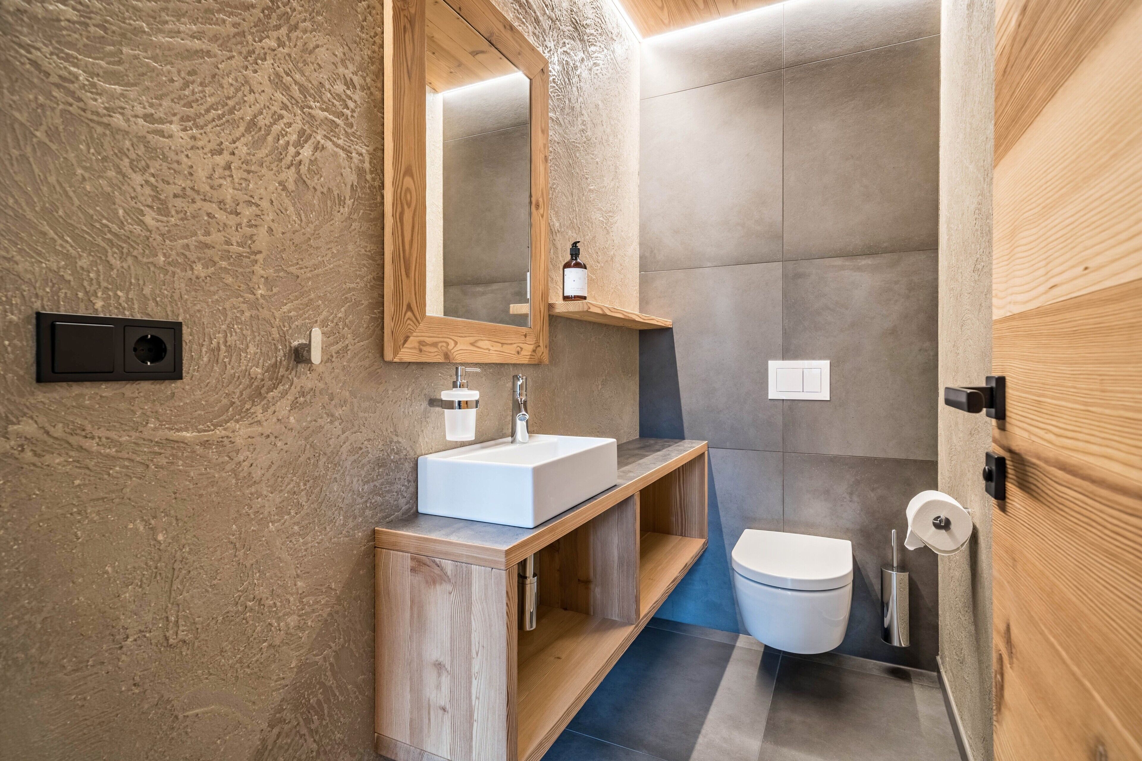 Une salle de bain avec un meuble-lavabo en bois, un lavabo blanc, un miroir, des toilettes et un espace douche.