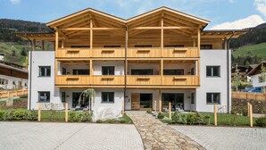 A two-story wooden building with balconies, a stone pathway, and a mountainous backdrop. - Apartment “Seebrunn - "Äußere Schwemmalm” with Mountain View, Wi-Fi and Sauna (Ulten)