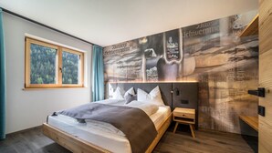 A modern bedroom with a bed, a small bedside table, a window, and a wall with a poster. - Apartment “Seebrunn - "Äußere Schwemmalm” with Mountain View, Wi-Fi and Sauna (Ulten)