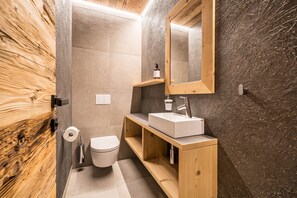 A modern bathroom with a wooden vanity, a white sink, and a large mirror.