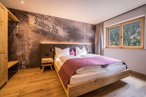 Une chambre à coucher avec un lit en bois, une table de chevet, une petite table, une fenêtre donnant sur une forêt et un mur orné de texte.