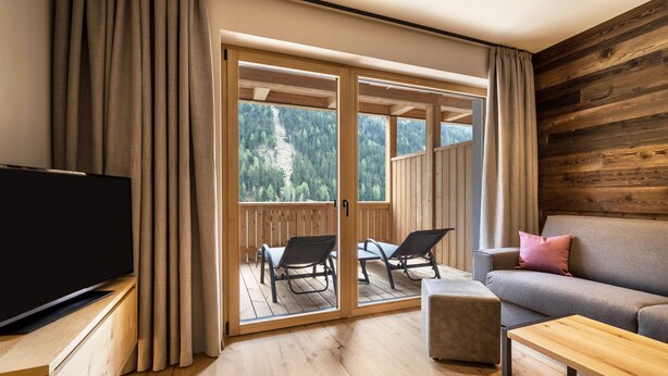 A room with a flat-screen TV, a sofa, a wooden coffee table, and a balcony with outdoor seating. - Apartment “Seebrunn - Kühberg Alm” with Mountain View and Lake View (Ulten)