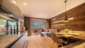 A modern kitchen with a large window, wooden wall paneling, and a dining area with a table set for two. - Apartment “Seebrunn - Kühberg Alm” with Mountain View and Lake View (Ulten)
