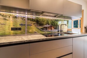 Une cuisine moderne dotée d’un îlot central intégré, d’appareils électroménagers en acier inoxydable et d’une fresque murale représentant un paysage de montagne.