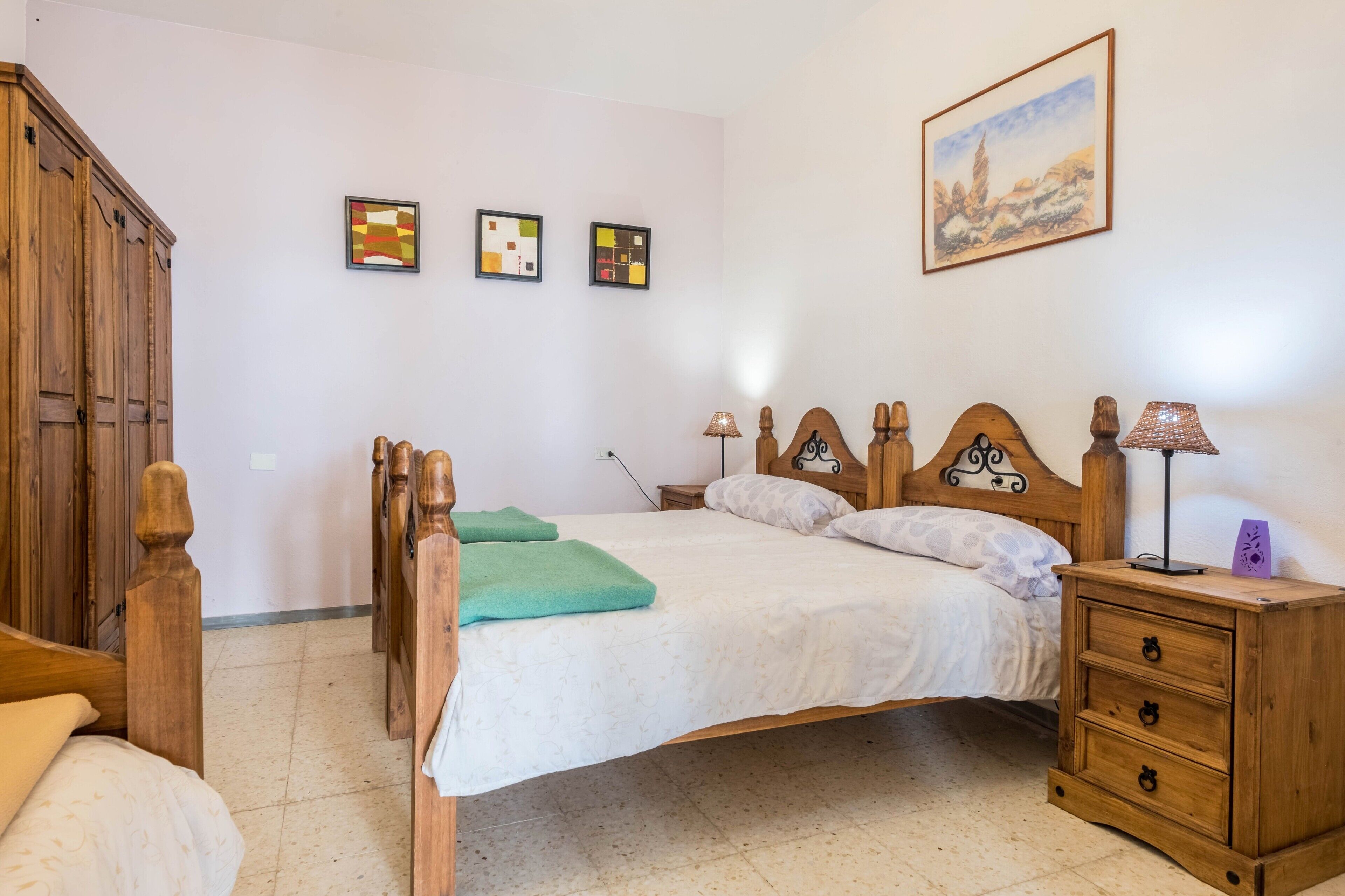 A bedroom with a wooden bed, a nightstand, a wardrobe, and three framed pictures on the wall.