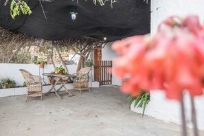 An outdoor patio with a table and chairs, a black umbrella, and potted plants.