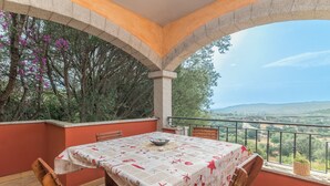 A terrace with a table set for dining, surrounded by stone arches, overlooking a landscape with trees and hills. - Holiday Home “Home Residence Barbara” with Garden & Balcony (San Teodoro)