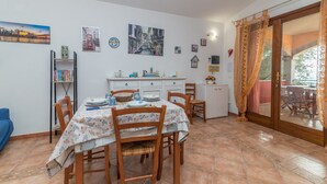 A dining area with a table set for four, a bookshelf, and a kitchen area with cabinets and a sink. - Holiday Home “Home Residence Barbara” with Garden & Balcony (San Teodoro)