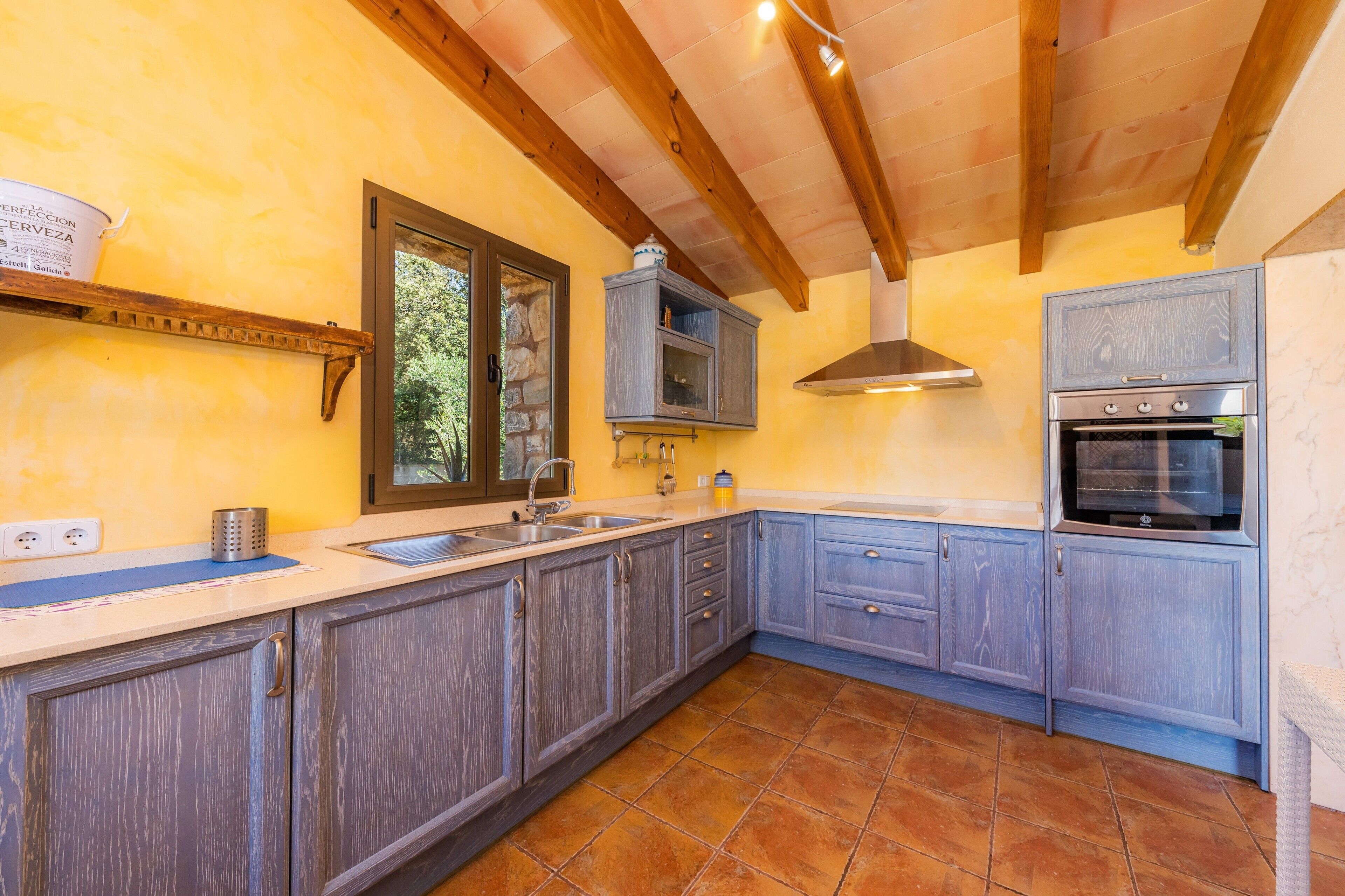 A kitchen with wooden cabinets, a built-in oven, a hanging light fixture, and a stone-framed window.