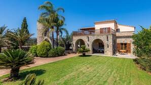 Una villa in stile mediterraneo con archi in pietra, un balcone e un prato curato.