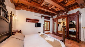 Una camera d'albergo con un letto grande, travi in legno al soffitto, una TV a schermo piatto e uno specchio.