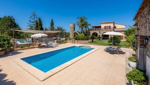 Una piscina con lettini, un edificio in pietra con un balcone e un giardino curato.
