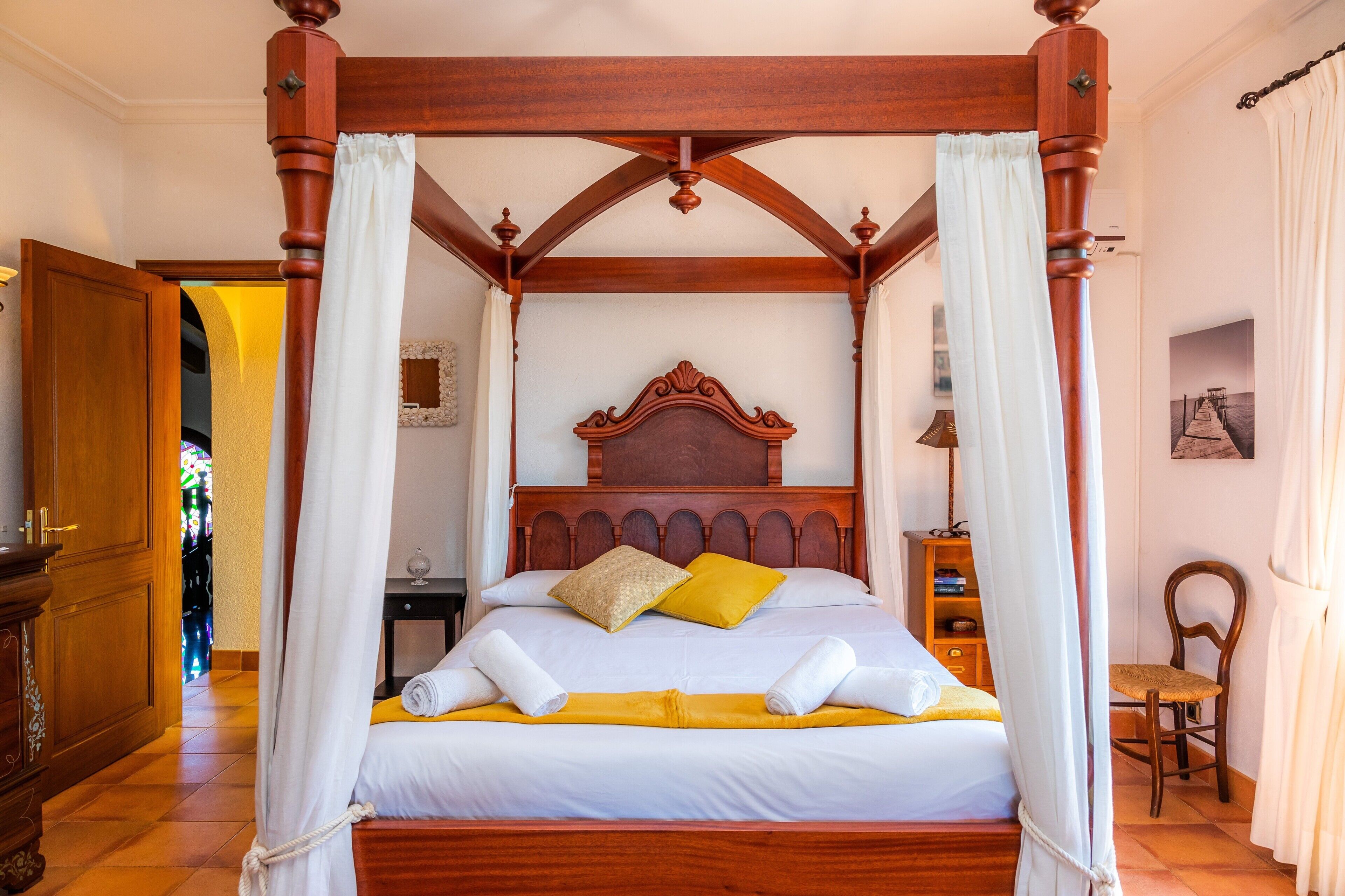 A four-poster bed with a canopy, a wooden headboard, and a bedside table with a lamp.