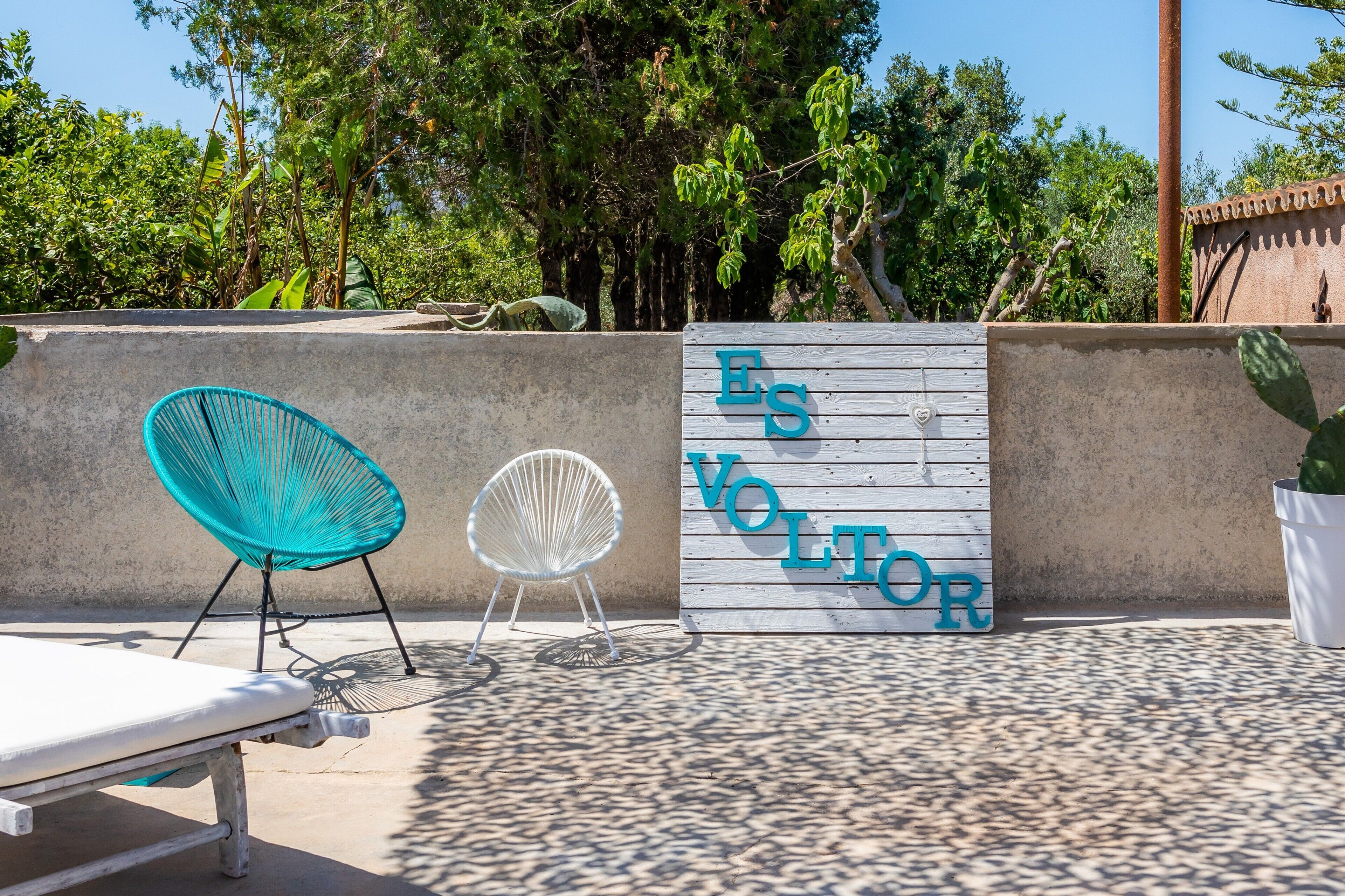 Ein Poolbereich mit einer weißen Liege, einem blauen Stuhl und einem Schild mit der Aufschrift 'ES VOLTOR'.