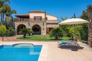 Ein Pool, ein Steinhaus und ein weißer Sonnenschirm.