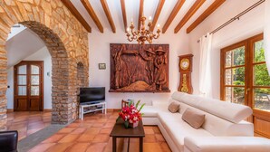 Un soggiorno con parete in pietra, travi in legno, un lampadario, un divano, una televisione e una sveglia.