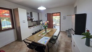 A modern kitchen with white cabinets, a dining table with chairs, and a refrigerator. - Villa "Giulia Grande" in rural area near the sea with mountain view and garden (Castiadas)