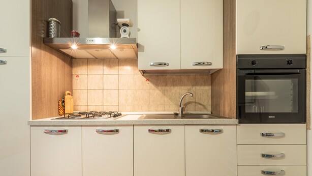 A modern kitchen with a gas stove, sink, oven, and wooden cabinets. - Villa "Giulia Grande" in rural area near the sea with mountain view and garden (Castiadas)