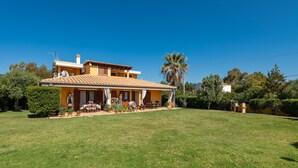 Une maison à deux étages dotée d’un patio, entourée d’une pelouse bien entretenue et de palmiers.
