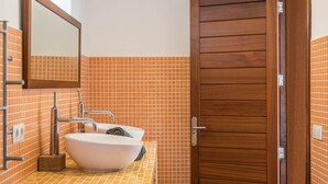 A bathroom with a wooden door, a white sink, and orange tiled walls.