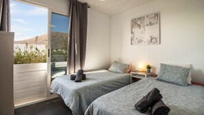 A bedroom with two beds, a window with curtains, a bedside table with a lamp, and a wall art piece.
