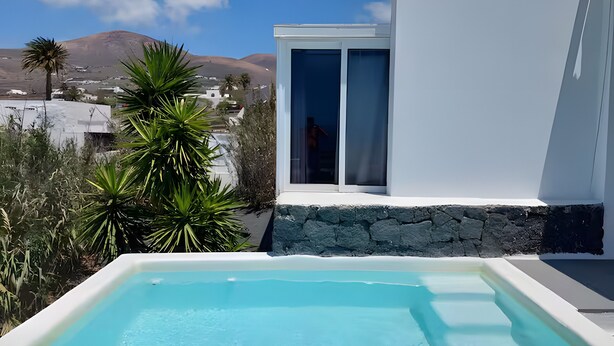 A modern pool with a clear view of the surrounding landscape, including a mountain and a white building with a stone base.