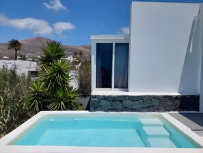 A modern pool with a clear view of the surrounding landscape, including a mountain and a white building with a stone base. - Holiday Apartment “Amanecer ” with Ocean and Mountain View, Terrace and Pools (Tías)
