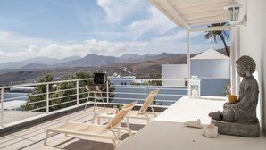 A balcony with a view of mountains, a Buddha statue, and a table with chairs.