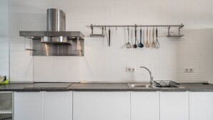 A kitchen with a stainless steel range hood, a hanging utensil rack, a double sink, and white cabinetry.