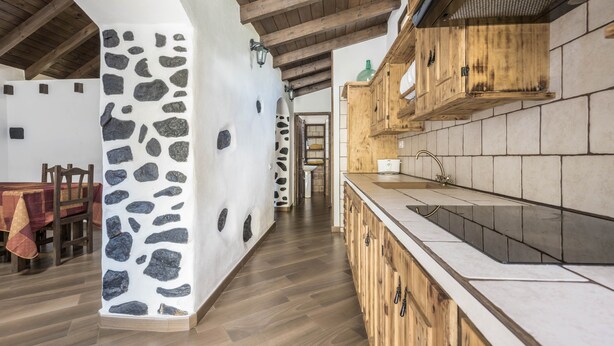 Eine Küche mit Holzausstattung, einer Wand aus Naturstein und einem Esstisch aus Holz mit Stühlen.