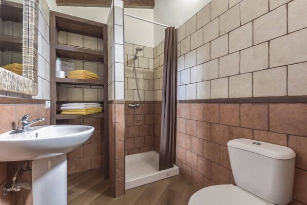 Un baño con lavamanos, ducha, inodoro y repisas con toallas.