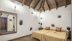 Ein Zimmer mit zwei Betten, Holzbalken an der Decke, einem Spiegel und Steindekorationen an den Wänden.