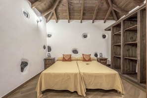 Una habitación con dos camas, vigas de madera, adornos en una pared de piedra y un armario de madera.