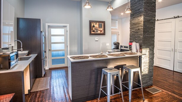 Une cuisine moderne dotée d’un îlot central, de tabourets de bar et d’un mur d’accent en pierre.