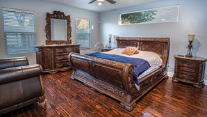 Une chambre à coucher avec un grand lit, des meubles en bois, un ventilateur de plafond et une fenêtre avec des stores.