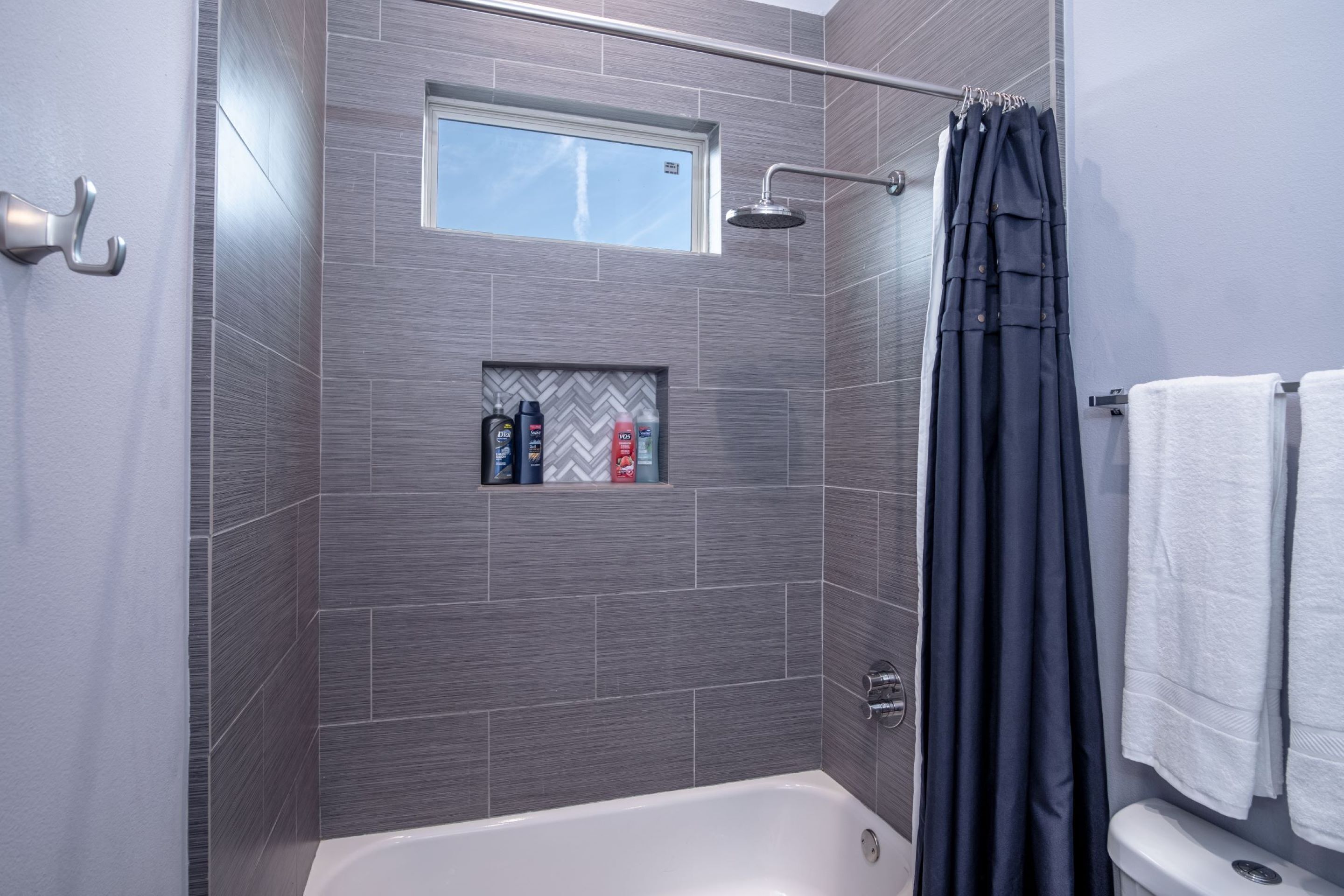 Un baño moderno con ducha, una ventana y un estante con artículos de tocador.
