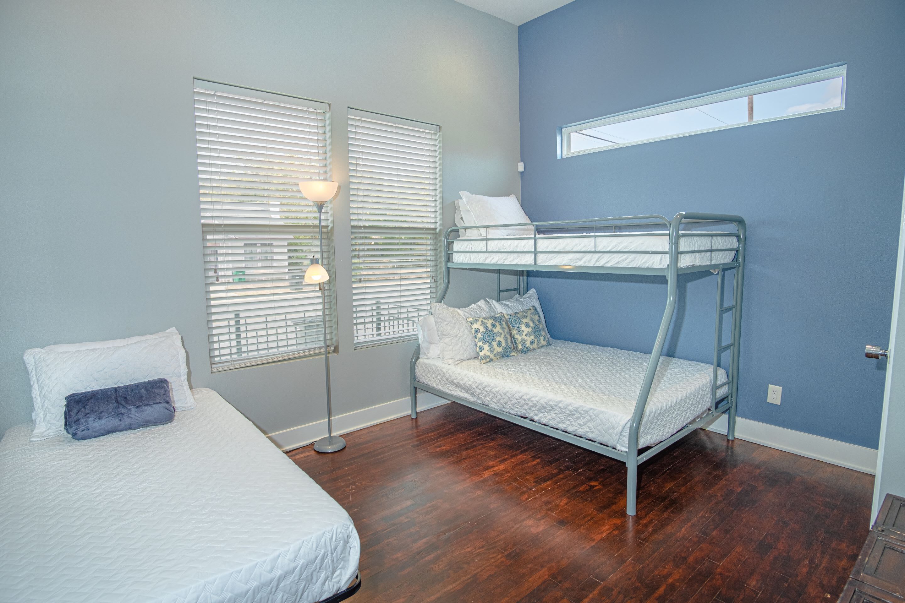 A bedroom with a bunk bed, a single bed, and a floor lamp.