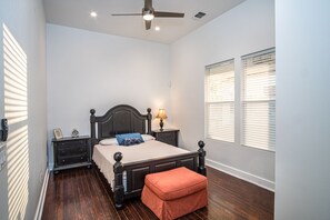 Ein Schlafzimmer mit Bett, Nachttischen, Deckenventilator und Fenster mit Jalousien.