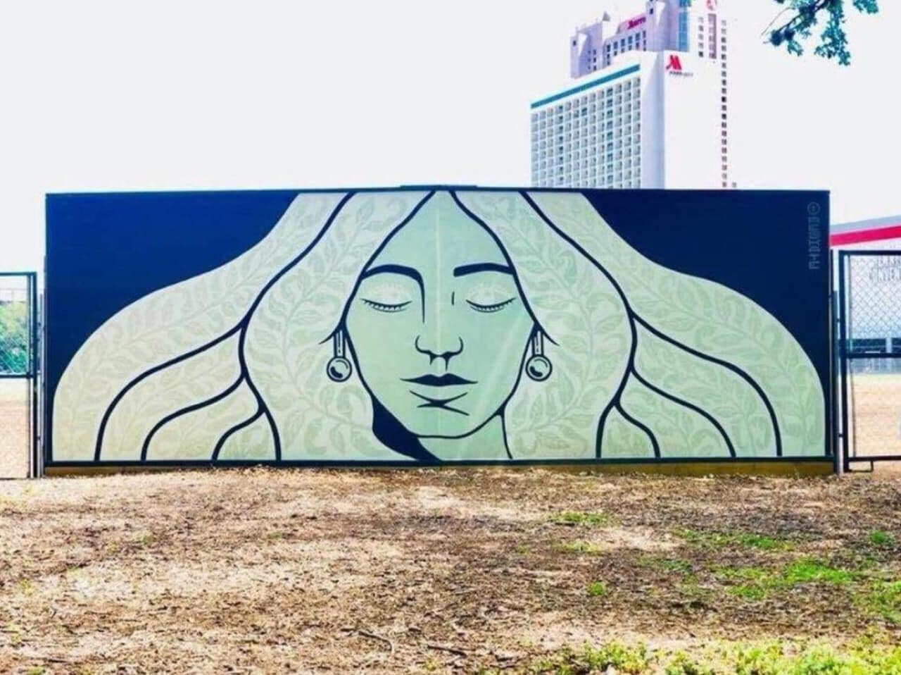 A large outdoor mural with a woman's face, surrounded by a fence.