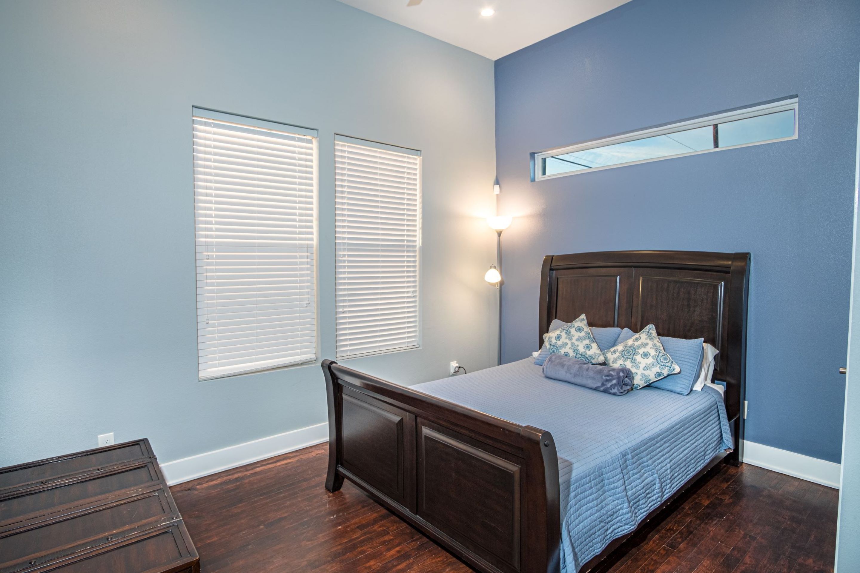 Un dormitorio con una cama de madera oscura, una pared azul y una ventana con persianas.