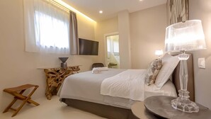Een moderne hotelkamer met een groot bed, een flatscreen televisie, een houten nachtkastje, een klein krukje en een decoratieve lamp.