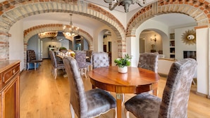 A dining area with a wooden table and upholstered chairs, brick arches, and a chandelier. - Ville Il Paradiso with Private Pools, Garden, Terraces, Ideal for Weddings (Panzano)