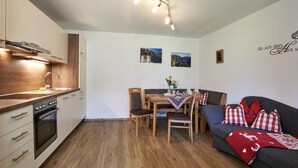 A modern kitchen with wooden cabinets, a built-in oven, and a dining area with a table and chairs. - Ferienwohnung Jenner, 2-4 Personen, Infrarotkabine, 65 qm, Balkon mit Bergblick (Schönau am Königssee)