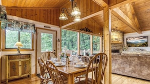 Comedor de madera con una mesa dispuesta para cuatro, rodeada de sillas, y una zona de cocina con chimenea de piedra.