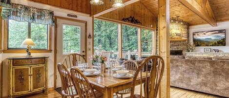 Ein Esszimmer aus Holz mit Tisch für vier Personen, umgeben von Stühlen, und ein Küchenbereich mit einem Kamin aus Stein.