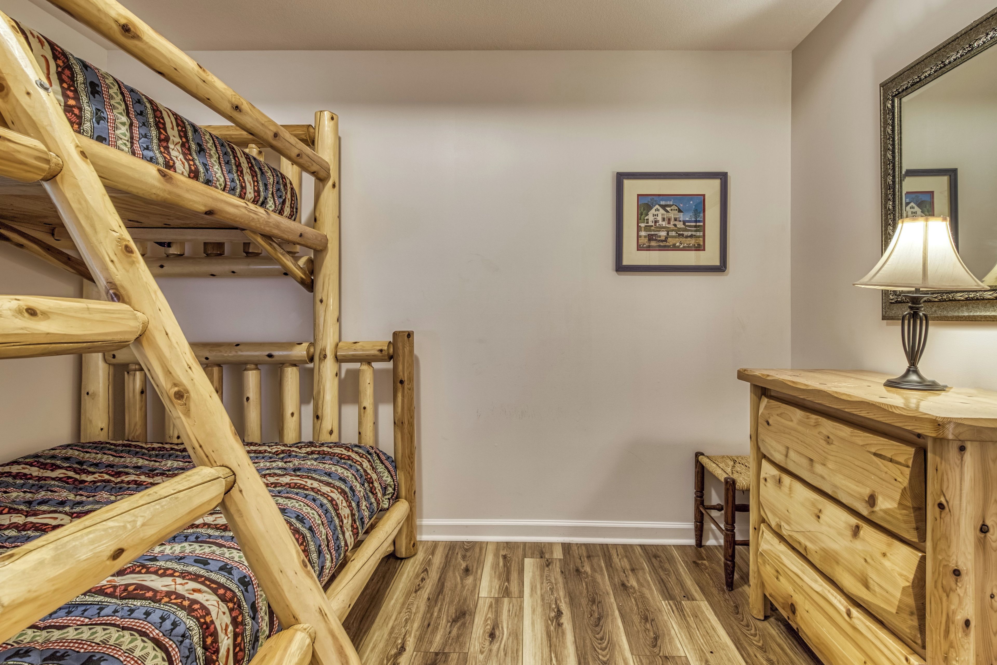 Ein Stockbett mit gemustertem Bettbezug, eine hölzerne Kommode, ein Spiegel und ein gerahmtes Bild an der Wand.