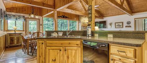 A wooden cabin interior with a kitchen featuring granite countertops, wooden cabinets, and a dishwasher.