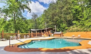 A swimming pool with a wooden deck, surrounded by trees and a small building with a roof. - Cabin w/Mountain Views-Pool Table-Private Hot Tub (Gatlinburg)